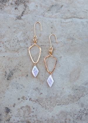 Gold shield shaped earrings with white diamond-shape pearls hanging from the bottom