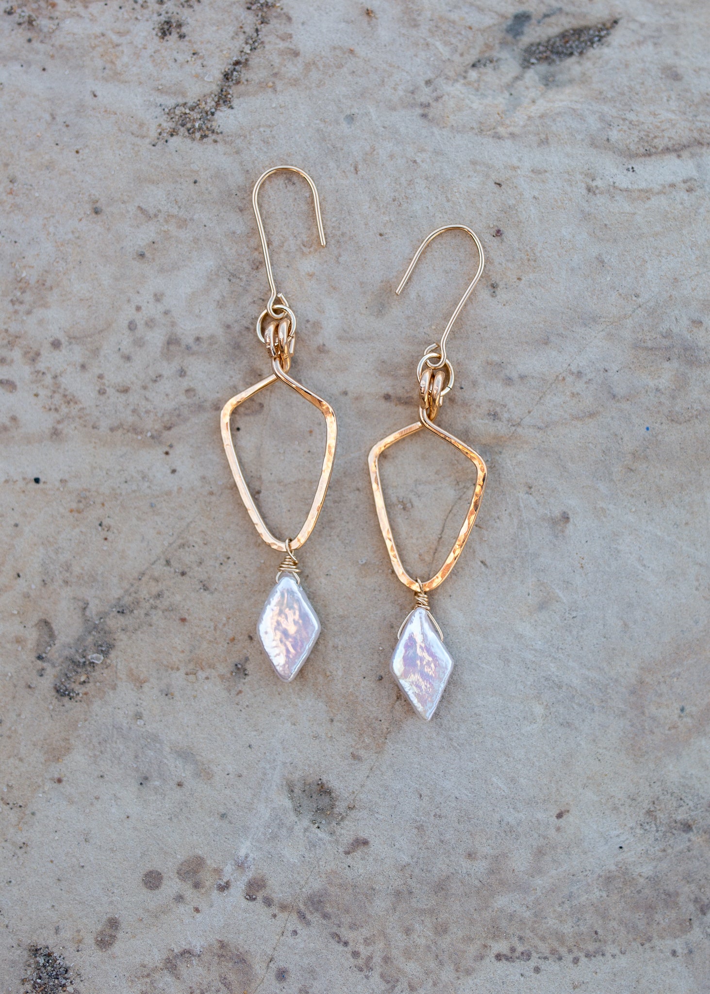 Gold shield shaped earrings with white diamond-shape pearls hanging from the bottom