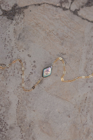 A necklace of gold dapped chain with diamond shaped iridescent pearl in line with the chain