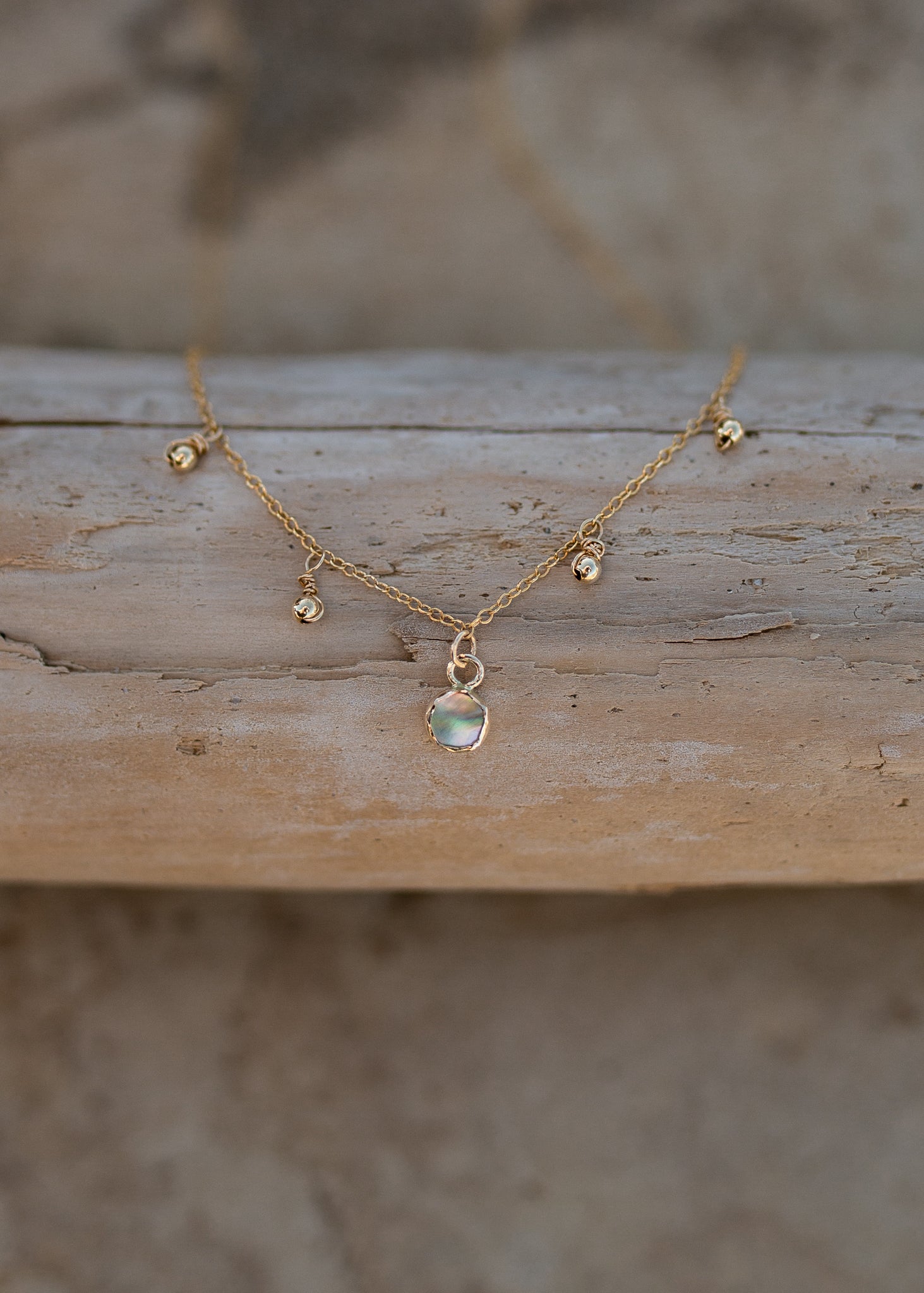 Dainty gold chain with four gold ball charms and a bezel set abalone piece in the center