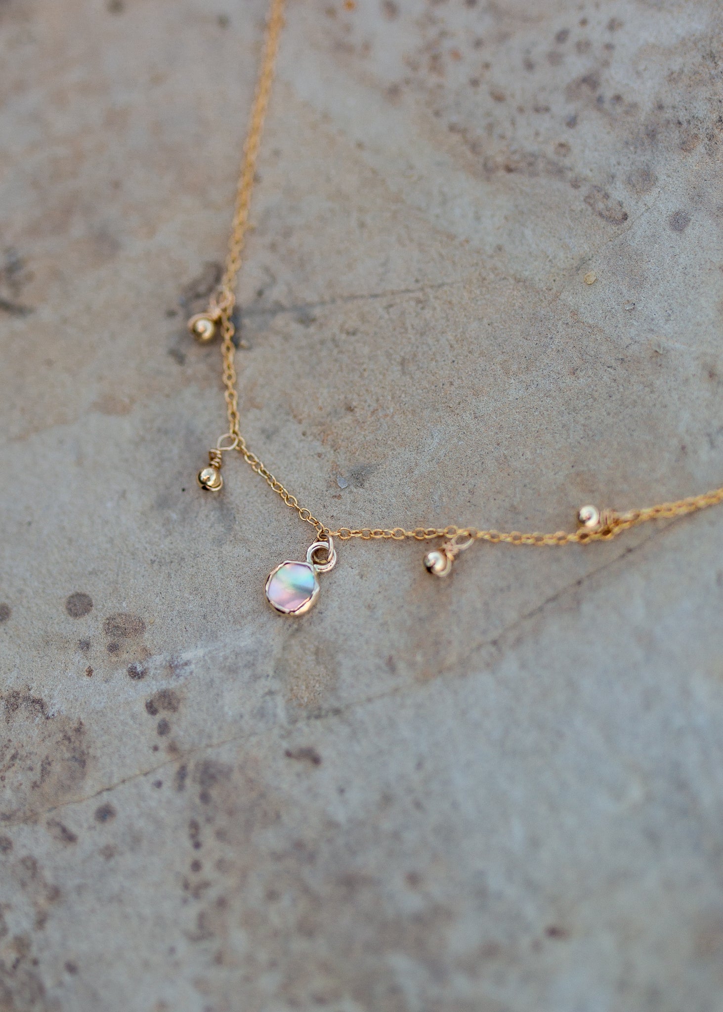 Dainty gold chain with four gold ball charms and a bezel set abalone piece in the center