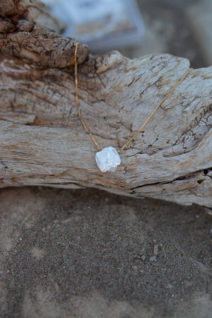 A necklace of white keishi pearl with gold venetian box chain, draped ver a piece of driftwood