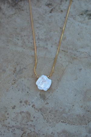 Dainty gold box chain with a large white keishi pearl pendant and a sandstone background