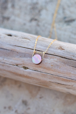 Mother of pearl necklace with gold bail and chain resting on a piece of driftwood