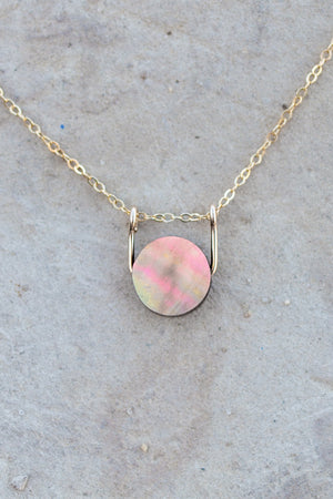 An up close view of the mother of pearl coin pendant, strung with a gold sliding bail on a dainty gold cable chain